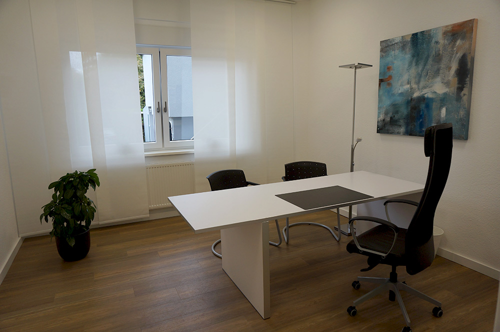 Büro 1 mit Schreibtisch, Stuhl und Fenster.